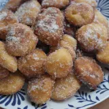 Montón de buñuelos de manzana dorados y espolvoreados con azúcar, servidos en un plato blanco con diseño azul.