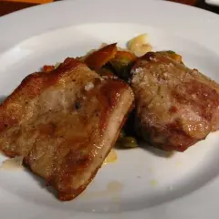 Dos trozos de secreto de cerdo a la plancha, dorados y jugosos, servidos con verduras salteadas en un plato blanco.