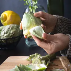 Manos preparan alcachofas para deliciosas recetas. Limón y aceite de oliva a la vista.
