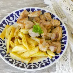 Raxo gallego jugoso con patatas fritas crujientes, servido en un plato con borde azul y blanco.