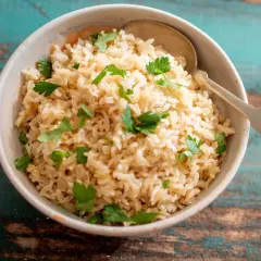 Un tazón de arroz integral esponjoso, perfecto para aprender como hacer arroz integral. Decorado con perejil fresco y una cuchara lista para servir.