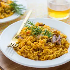 Delicioso arroz con secreto ibérico y setas, adornado con romero fresco. Un plato reconfortante y lleno de sabor.