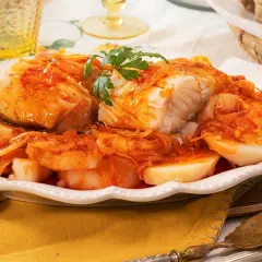 Bacalao a la gallega, un plato tradicional con trozos de pescado blanco cubiertos de una salsa rojiza con cebolla y patatas cocidas.