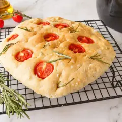 Focaccia receta casera con tomates cherry y romero sobre una rejilla.