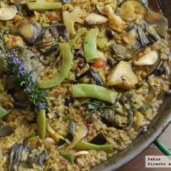 Paella de verduras vibrante, con alcachofas, calabacín, pimientos y romero fresco. Un festín para la vista y el paladar.