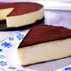 Un delicioso pastel de queso cubierto de cacao, perfecto para postres fáciles. Una rebanada servida en un plato con flores azules.