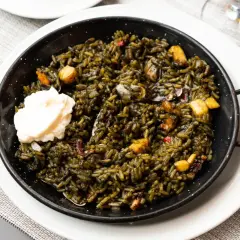 Arroz negro con sepia, servido en paellera con una cucharada de alioli. Se aprecian trozos de sepia y pimientos.