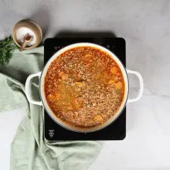 Olla con lentejas con arroz y zanahoria hirviendo. Al lado, perejil fresco y un cuenco de sal.