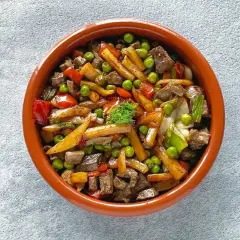 Un sabroso frito mallorquín con trozos de carne, patatas, guisantes y pimientos en una cazuela de barro.