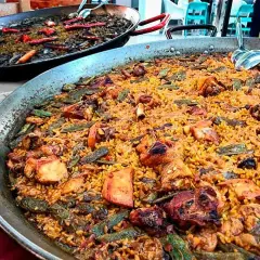 Paella valenciana con pollo, conejo y verduras. Los ingredientes se mezclan con el arroz en esta gran paellera.