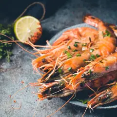 Gambones al horno, jugosos y dorados, servidos con hierbas frescas y rodaja de limón.