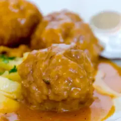 Albondigas a la jardinera, jugosas y cubiertas de salsa, acompañadas de patatas y perejil. Un plato casero listo para disfrutar.