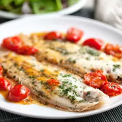 Dos filetes de lenguado a la plancha, servidos con tomates cherry salteados y perejil picado.
