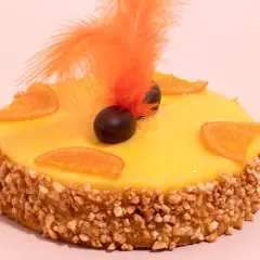 Deliciosa mona de Pascua catalana con glaseado amarillo, rodajas de naranja, chocolate y plumas naranjas.
