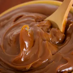 Cuchara de madera removiendo un tazón lleno de dulce de leche cremoso, perfecto para tu dulce de leche receta.