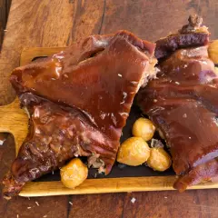 Delicioso cochinillo al horno, receta de la abuela, servido con patatas asadas sobre tabla de madera.