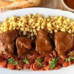 Delicioso jarrete de ternera estofado, acompañado de patatas fritas crujientes y zanahorias en rodajas.