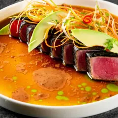 Tataki de atún sellado, servido en un caldo vibrante con aguacate, zanahoria rallada y un toque picante.