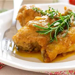 Pollo en salsa de la abuela, jugoso y dorado, servido en plato blanco con romero fresco. Un clásico casero.