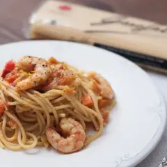 Espaguetis con gambas y trocitos de tomate, servidos en un plato blanco. Un tenedor plateado descansa a la derecha.