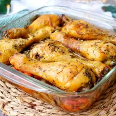 Muslos de pollo al horno dorados y jugosos, sazonados con hierbas aromáticas, servidos en una fuente de vidrio.