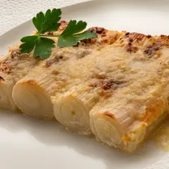 Tres tiernos puerros al horno gratinados con queso, coronados con una ramita de perejil fresco.