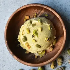 Cremoso helado de pistacho, adornado con trozos de pistacho, servido en un cuenco de madera rústico.