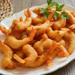 Un plato blanco lleno de gambas a la gabardina doradas y crujientes, decorado con perejil fresco.