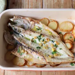 Lubina a la espalda horneada con patatas y ajo, lista para servir.