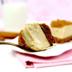 Un trozo cremoso de tarta de lotus en una cuchara dorada, con otra porción al fondo y un vaso de leche.