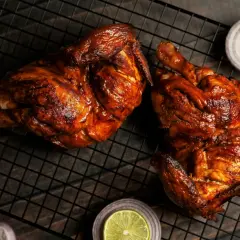 Dos jugosos pollos a la brasa, dorados y listos para disfrutar, acompañados de rodajas de cebolla roja y limón.