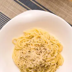 Un plato de cacio e pepe, pasta cremosa con queso y pimienta negra, servido en un cuenco blanco sobre un mantel a rayas.