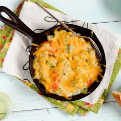 Coliflor gratinada burbujeante en sartén de hierro fundido, lista para disfrutar con pan crujiente.
