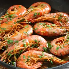 Gambones al ajillo chisporroteando en una sartén, con perejil fresco espolvoreado. ¡Un plato delicioso!