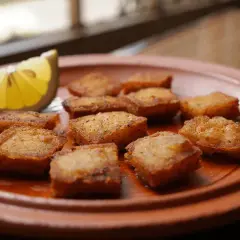 Deliciosos trozos de bacalao rebozado, dorados y crujientes, servidos en un plato de barro con una rodaja de limón.