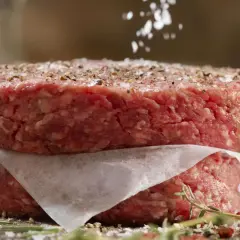 Dos hamburguesas de carne picada apiladas, sazonadas con sal y pimienta.