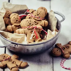 Un cuenco lleno de galletas de jengibre con forma de hombrecito, algunas atadas con hilo rojo y blanco.