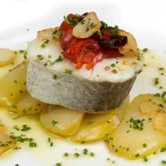 Deliciosa merluza a la plancha sobre patatas, con pimientos asados, ajo crujiente y perejil picado.