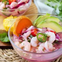 Delicioso ceviche de gambas con aguacate, cebolla morada, chile jalapeño y tomate. Servido en un cuenco de cristal, acompañado de maíz y cilantro fresco.