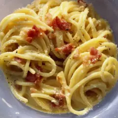 Un plato de pasta carbonara cremoso con trozos de panceta crujiente y espolvoreado con queso rallado.