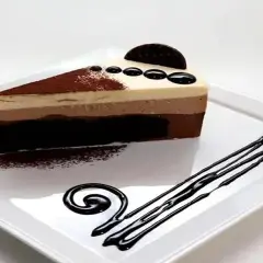 Una rebanada de tarta de tres chocolates, con capas de chocolate blanco, con leche y negro, decorada con cacao en polvo y un disco de chocolate.