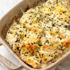Bacalao a la nata gratinado, cubierto con semillas negras y eneldo, burbujeando en una fuente de cerámica.