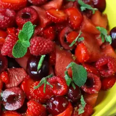 Delicioso postre con fresas, frambuesas, cerezas y menta en un tazón amarillo.