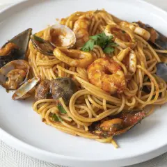 Espaguetis a la marinera con gambas, mejillones, almejas y calamares, servidos en un plato blanco.