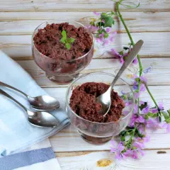 Dos copas de delicioso mousse de chocolate, decoradas con menta y flores moradas, listas para disfrutar.