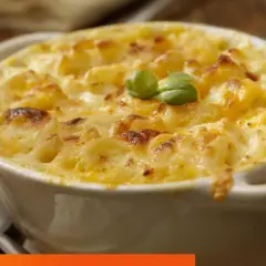 Un plato cremoso de macarrones con queso, gratinado y decorado con una hoja de albahaca.