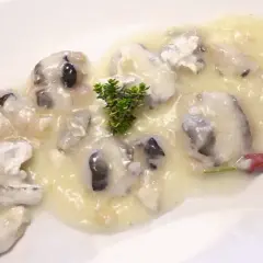 Deliciosas cocochas de merluza en salsa cremosa, adornadas con una ramita de tomillo y un toque de pimiento rojo.