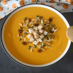 Un cremoso puré de calabaza adornado con picatostes, nueces, pasas y semillas de calabaza.