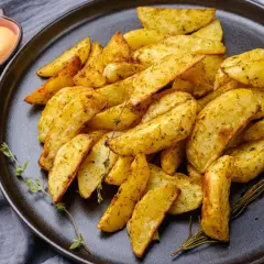 Patatas fritas al horno doradas y crujientes, sazonadas con hierbas, servidas en un plato oscuro con una salsa cremosa y romero fresco.