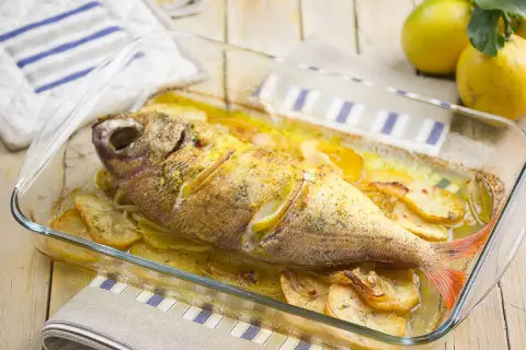 Besugo al horno con patatas y limón, recién sacado del horno en una fuente de cristal.